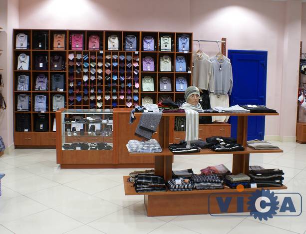 Торговое оборудование для продажи одежды включает в себя островной стеллаж, прилавок для одежды и пристенный стеллаж под рубашки и галстуки.